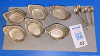 Group of six sterling nut dishes and four decorative spoons displayed on grey pad with lot card