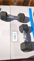 Two 15 pound black hex dumbbells with chrome knurled handles placed on a white surface.