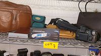 Photo showing multiple brown and black leather bags, a digital thermometer in a box, and a digital camera on a metal shelf.