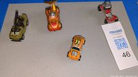 Four vintage collectible toy cars arranged on a surface including two orange hot rod cars, one yellow-green jeep, and a red motorbike with figures.