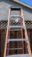Front view of the Werner 7 foot fiberglass step ladder showing the orange fiberglass rails, metal braces, and black plastic top with Werner logo