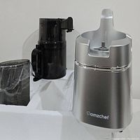 Silver base unit of AMZCHEF juicer with clear juice and black pulp containers in packaging.