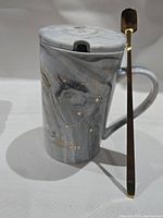Front view of ceramic coffee cup with lid and long gold spoon.