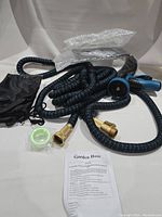 Full view of coiled expandable garden hose with brass connectors, Teflon tape, spray nozzle, and instruction sheet on white background.