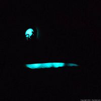 Bookmark glowing in the dark showing the skull charm and feather shape glowing.