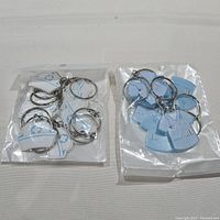 Two sealed transparent plastic bags containing new light blue medical uniform shaped keychains with printed medical designs.