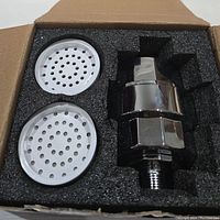 New shower head filter and two white perforated screens packed in foam in a box.