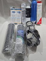 Photo of various water filter cartridges in boxes and wrapped in bubble wrap along with a black plastic accessory and a Frigidaire filter box