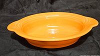 Side view of bright orange oval casserole dish showing shape, handles and interior detail