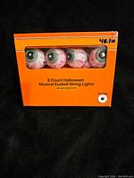 Box front side showing 8 eyeball string lights with green irises and red veins, with text detailing product as 8 count Halloween musical eyeball string lights, 80 inches long.