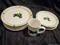 Photo showing stacked John Deere large and smaller plates along with a mug, all featuring green John Deere tractors and yellow wheat design around rims.