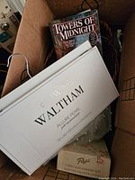 Box with 'Waltham Allure Pearl' drawer liner box, 'Towers of Midnight' book, wicker basket and some coiled cords inside.