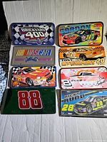 Photo showing 8 vintage NASCAR license plates including Brickyard 400, Jeff Gordon #24, Tony Stewart #20, Dale Earnhardt Jr. #8, Ricky Rudd #28, McDonald's themed, Ken Schrader #88, and one background green plate with number.