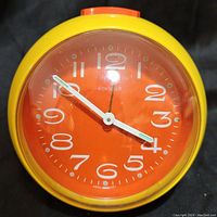 Front view of vintage 'Best Ever' alarm clock showing orange face, white numbers, and hands inside yellow casing with clear plastic cover.
