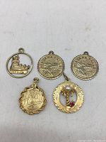 Photo showing all five assorted gold tone vintage souvenir pendants arranged flat on a white background.