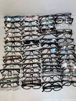 Top-down view of 43 assorted glasses and optical frames arranged in rows showing variety of colors and styles.