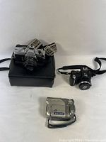 Three cameras displayed: Minolta SRTMC-II 35mm film camera with attached lens and case on the left, Kodak EasyShare P850 digital camera on the right, and Canon DC40A digital video camera in front