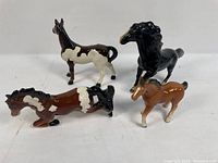 Four ceramic horse figurines displayed together showing various poses and colors, including brown, black, and white.