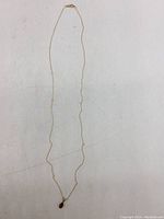 Full view of the delicate gold chain necklace with garnet pendant laid out straight for overall length and condition.