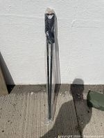 Two black SportCamZ SCX-MULATI poles wrapped in clear plastic against a white wall, standing upright on the ground.