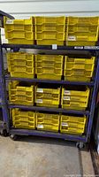 Full view of purple metal shelving cart with twelve yellow plastic storage boxes on four shelves.