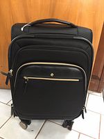 Front view of the black Samsonite suitcase highlighting multiple zippered compartments and front pocket with gold-tone zipper pulls