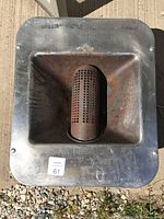 Top view of the metal square burner with cylindrical perforated burner in the center, showing signs of rust and wear.