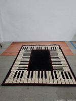 Full view of the rectangular rug showing piano key pattern with black center and red border.