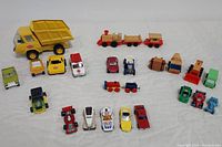 Collection of vintage toys including dump truck, wooden train cars, and various small toy cars and trucks arranged on white background.