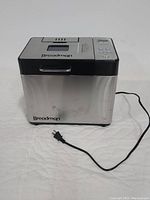 Full side view of Breadman bread maker showing stainless steel body and black accents, including power cord plugged out.