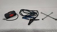 Overview of the car care items spread out on a white surface: the air pump, charging cables, and tire iron.