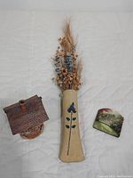 Photo showing pottery wall vase with dried flowers, Windy Meadows pottery house, and Thomas Kincaid 3D magnet on white background.