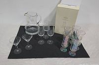 Full lot view showing multiple glassware items placed on black background, including Fluted Lenox glasses in box, iridescent parfait glasses, various etched stemware and the pitcher.