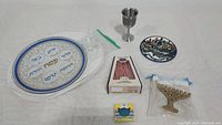 Photo showing all items of the Judaica set arranged on a table including Seder plate, Kiddush cup, Jerusalem plate, Menorah and candles.