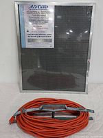 Photo of Electra Silver anti-microbial electrostatic air filter with label detailing features and heavy duty orange extension cord coiled on table.