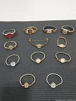 Twelve ladies watches arranged on a black surface showing a variety of metal tones and band styles including stretch and bangle types.