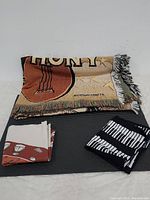 Woven blanket folded with table runner and fabric piece displayed on black surface