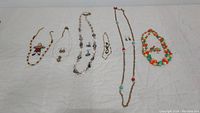 All six necklace sets displayed on a white cloth. Each set includes necklaces and some have matching earrings. Varied bead materials including wood, glass, and metal.