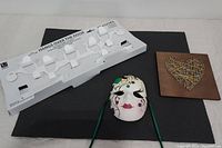 Lot overview showing all three items on a black mat: over the door hanger, Mardi Gras mask, and wooden love plaque.