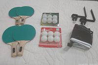 Overall view of 4 green paddles, 2 packs of unopened white balls, black mesh net and clamp supports on white background.