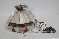Photo of the Tiffany style stained glass pendant light wrapped partially in plastic, includes metal ceiling fixture and chain.