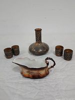 Wide shot showing the vintage Holt Howard decanter with four matching cups and porcelain gravy boat with sturgeon fish design on a white quilted surface.