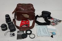 Image showing entire camera set including brown leather camera bag, two lenses, manual, lens caps, additional accessories such as blower bulb, shutter release cable, and camera case.