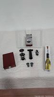 Full view of all wine accessories displayed on white surface: wire baskets, corkscrew, vacuum pump, wooden stoppers box, corksicle box, aerator and wine pourer.