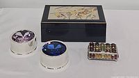 Four decorative boxes arranged on white background: wooden box with floral inset, two round trinket boxes with purple and blue faceted gem tops, and a multi-colored vintage jewelry box with faceted gem panels.
