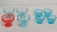 Front view of 4 aqua blue floral embossed ice cream cups and 4 blue glass dessert dishes with scalloped edges.