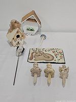 Photo showing white bird feeder, beige angel birdhouse, three angel garden stakes, slate welcome sign with bunny and floral design, and mushroom garden stake