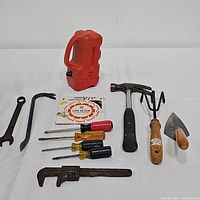 Overview of assorted used tools on white background including hammers, wrenches, screwdrivers, saw blade, and measuring tape