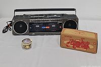 Photo showing JVC RC-W3 radio cassette recorder, vintage round music box, and ERTL 1937 Ahrens-Fox firetruck box on white background.