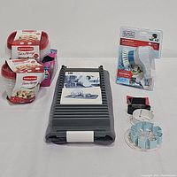 Photo showing all items in the lot including Black & Decker grimebuster scrubber in packaging, snowman cookie cutter, dish rack with mat, two boxes of Rubbermaid bowls, and a box of Ziploc tabletop storage bags.
